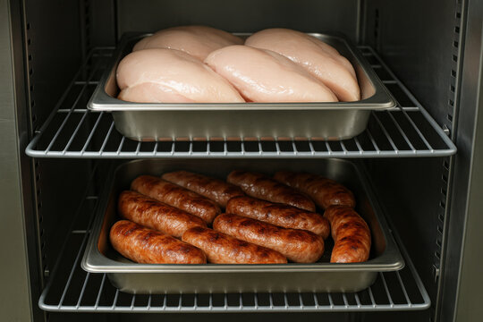 Raw chicken breast stored above cooked sausage on wire rack shelf creating cross contamination hazard demonstrating unsafe food handling practice in commercial kitchen