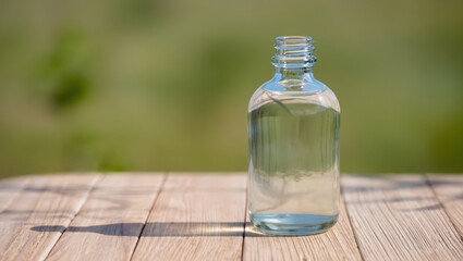 Delicate glass bottle holding clear water glistens under a soft sunlit backdrop in a tranquil garden scene