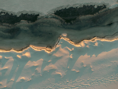 Frozen shoreline shows ice patterns and tracks at sunset