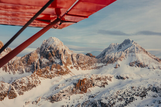 Red airplane wing framing snow covered mountain peaks at sunset.