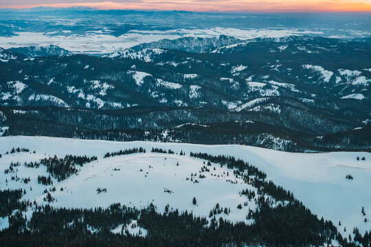 Snow covered hills and forest at dusk under soft winter light.