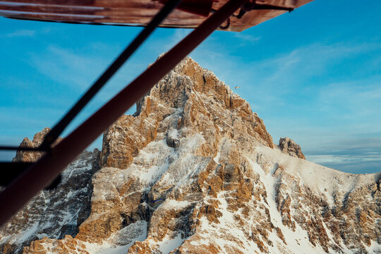 Snow covered mountain peak framed by an airplane wing at sunset.