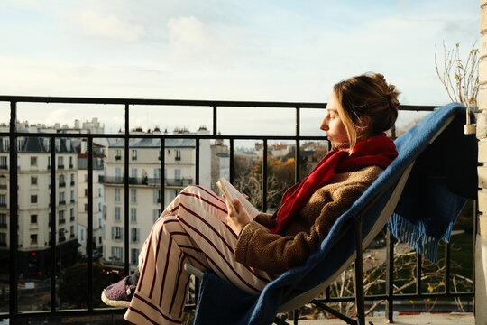 Woman Reading Book on Balcony Overlooking City