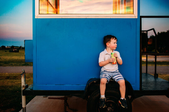 Boy sitting on trailer with drink watching sunset