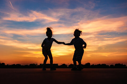 Silhouette of two children holding hands at sunset