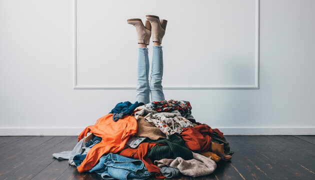 Messy pile of clothes with legs sticking out in a room with wooden floor and plain walls during the day
