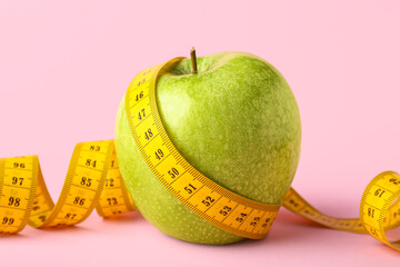 Green apple with yellow measuring tape on pink background. Diet concept