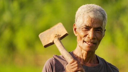 Portrait, smiling elderly man asian farmer with shovel on flores island, indonesia, indonesian people, in agricultural field, grey hair, missing tooth, southeast asia © Spice Footage
