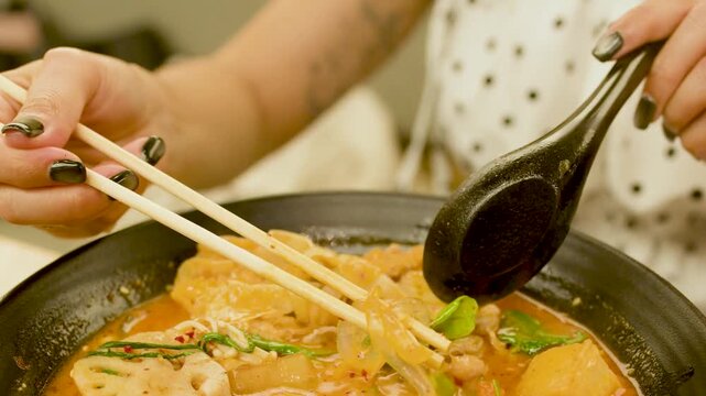 Close Up of Woman Lifting Glass Noodles From Spicy Asian Soup