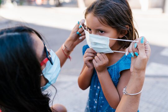 Close-up of mother wearing face mask to daughter on street