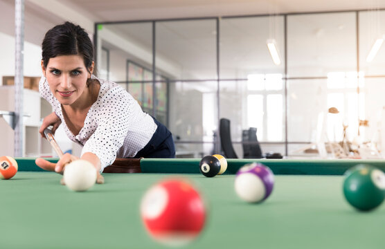 Determined businesswoman playing pool billard in modern office