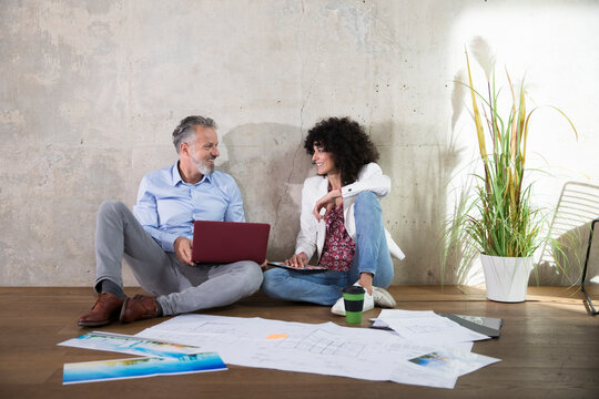 Businessman and businesswoman sitting on the floor in a loft working with laptop and documents