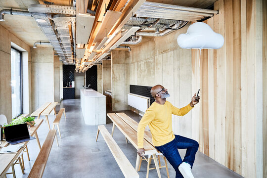 Mature businessman holding cell phone attached to cloud balloon