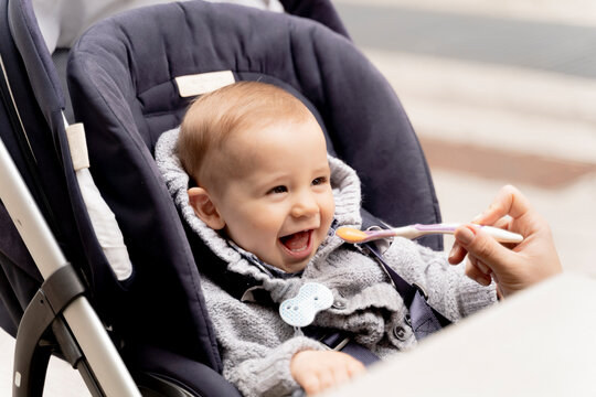 Mother feeding laughing baby boy in stroller