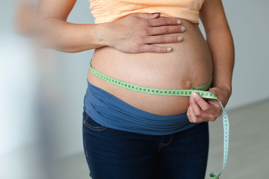 Young pregnant woman measuring her baby belly