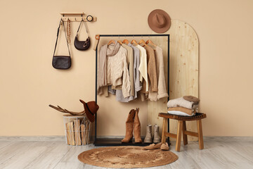 Rack with knitted sweaters, shoes and firewood near beige wall in room