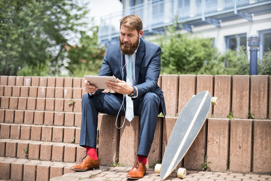 Businessman with skateboard using tablet and earphones