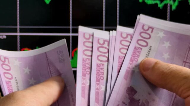 Hands count several 500 euro banknotes before the stock market chart.