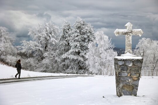 une femme marche sur la neige devant une croix de J&eacute;sus