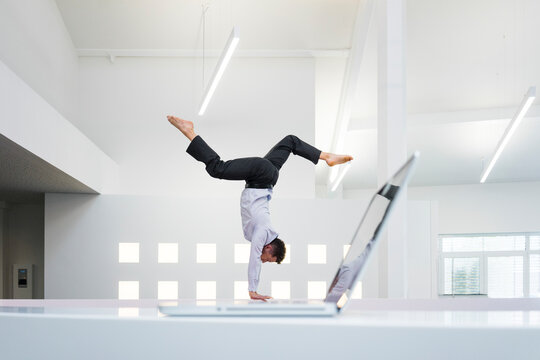 Businessman doing a handstand at laptop in office