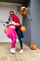 Obraz premium African American mother and daughter hugging and posing on porch, holding orange pumpkin buckets
