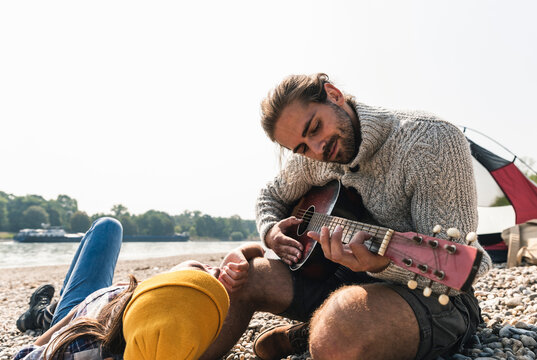 Happy young couple playing guitar at a tent at the riverside