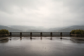 A wet road with a guardrail and a foggy mountain range in the background on a rainy day.