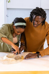 African American couple making dough at white counter, cutting with pizza cutter, rolling pin © wavebreak3
