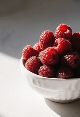Fresh raspberries piled high in a white bowl, bathed in soft natural light