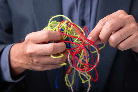 Businessperson untangling messy threads, symbolizing solving complex problems, conflict resolution, decision making, organization and finding clarity in business challenges