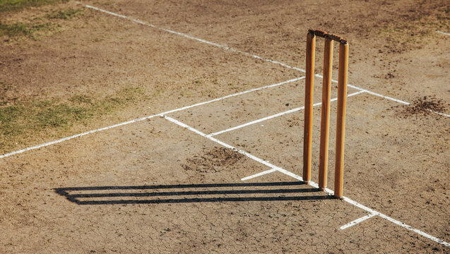Wooden cricket stumps on a dry field with marked pitch lines