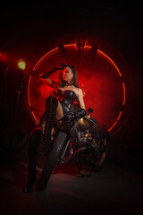 Fototapeta na wymiar Stylish beautiful young woman in black leather corset and boots posing on vintage motorcycle on old garage dark interior background.