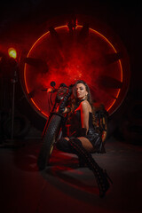 Fototapeta na wymiar Stylish beautiful young woman in black leather corset and boots posing on vintage motorcycle on old garage dark interior background.