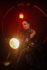 Naklejka na ściany i meble Stylish beautiful young woman in black leather corset and boots posing on vintage motorcycle on old garage dark interior background.