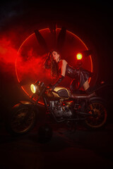 Fototapeta na wymiar Stylish beautiful young woman in black leather corset and boots posing on vintage motorcycle on old garage dark interior background.