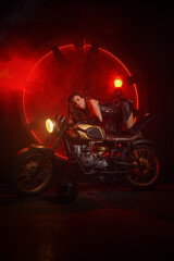 Fototapeta na wymiar Stylish beautiful young woman in black leather corset and boots posing on vintage motorcycle on old garage dark interior background.