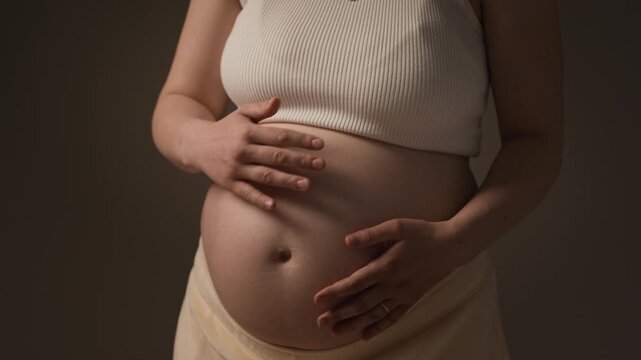 Dolly-out portrait of young Caucasian pregnant woman embracing her belly during maternity session, expressing calm, connection and anticipation of motherhood