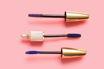 Fototapeta premium Different brushes of blue mascara on pink background, closeup