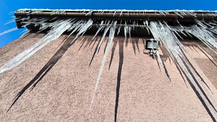 Icicles of ice hang from a roof gutter and a floodlight © john1179