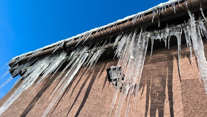 Icicles of ice hang from the roof drainpipe of a house and a floodlight © john1179