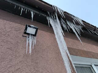 Large long icicles of ice hang from the gutter of a house roof © john1179