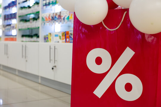 Sign with percentage and background of shelf full of medications. Sale at pharmacy. Concept to create affordable medications for population. Purchase of painkillers and medications for elderly