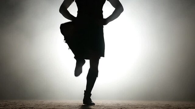 A lone silhouette demonstrating the energetic and intricate footwork characteristic of traditional irish dancers on a smoky stage.