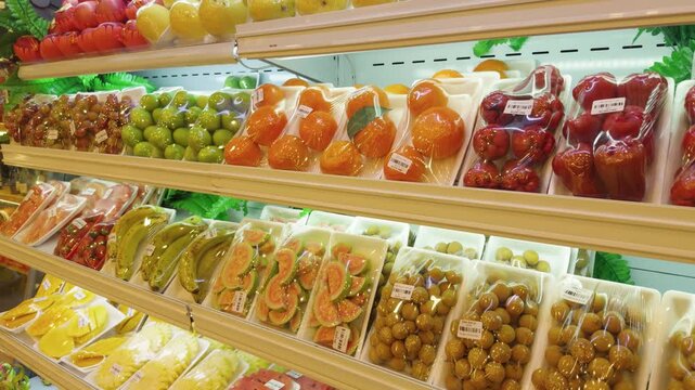 Grocery store shelves displaying an assortment of fresh tropical fruits and produce, neatly packaged in plastic wrap and styrofoam trays within a refrigerated display in da nang