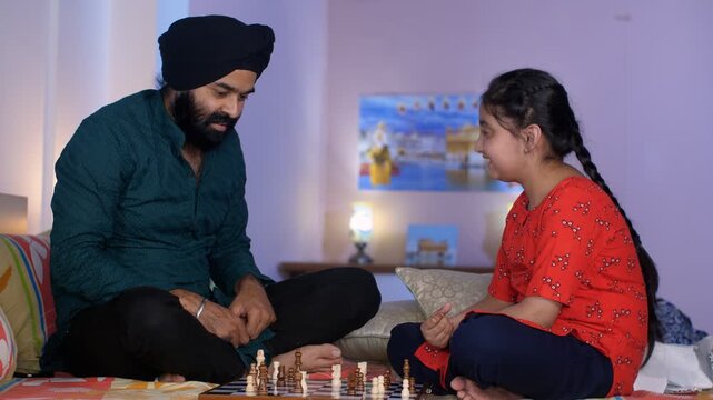 Indian father-daughter playing a board game - playing chess  checkmate  squabbling  mind game. A pretty young girl defeats her dad while playing chess - a strategic move  competitive game  a Sikh f...