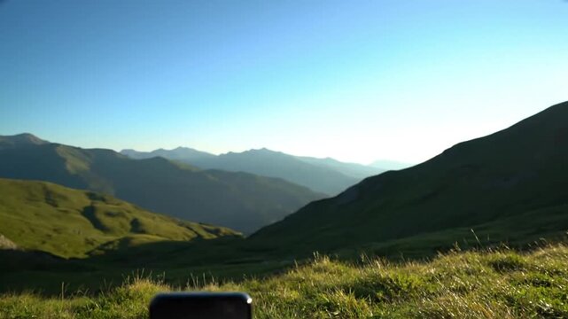 A sleek, generic smartphone is thoughtfully positioned in the vibrant green foreground, capturing a breathtaking panoramic vista of majestic mountain ranges under a pristine, gradient blue sky. The ea