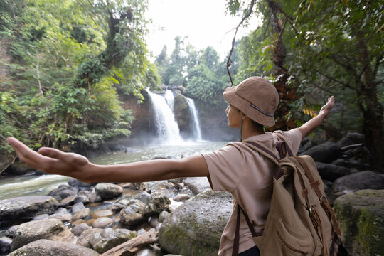 Asian teenage boy hiking at tropical waterfall with arms outstretched