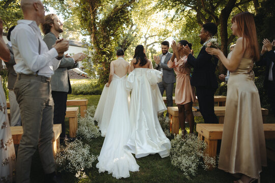 Two brides walking down the aisle surrounded by joyful wedding guest applause