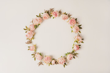 Elegant circular floral wreath composed of soft pink roses and green branches on cream colored backdrop