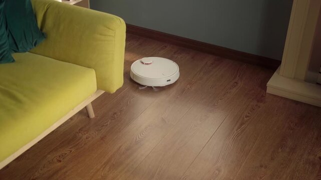 White robot vacuum cleaner navigating a modern living room, cleaning the wooden floor surfaces while providing smart home automation and convenience in daily domestic life